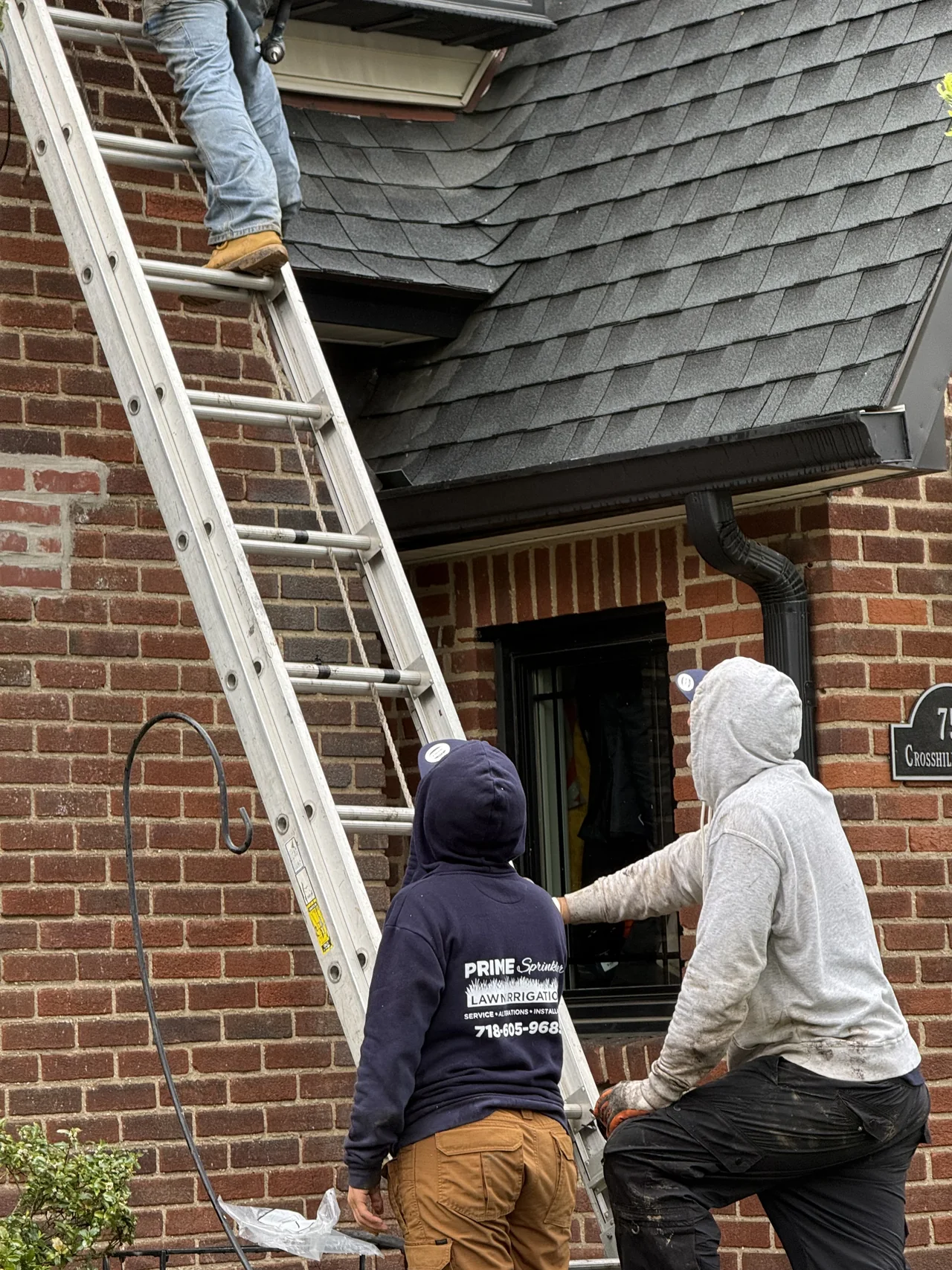 Prime Sprinkler technician working with ladder access near a home