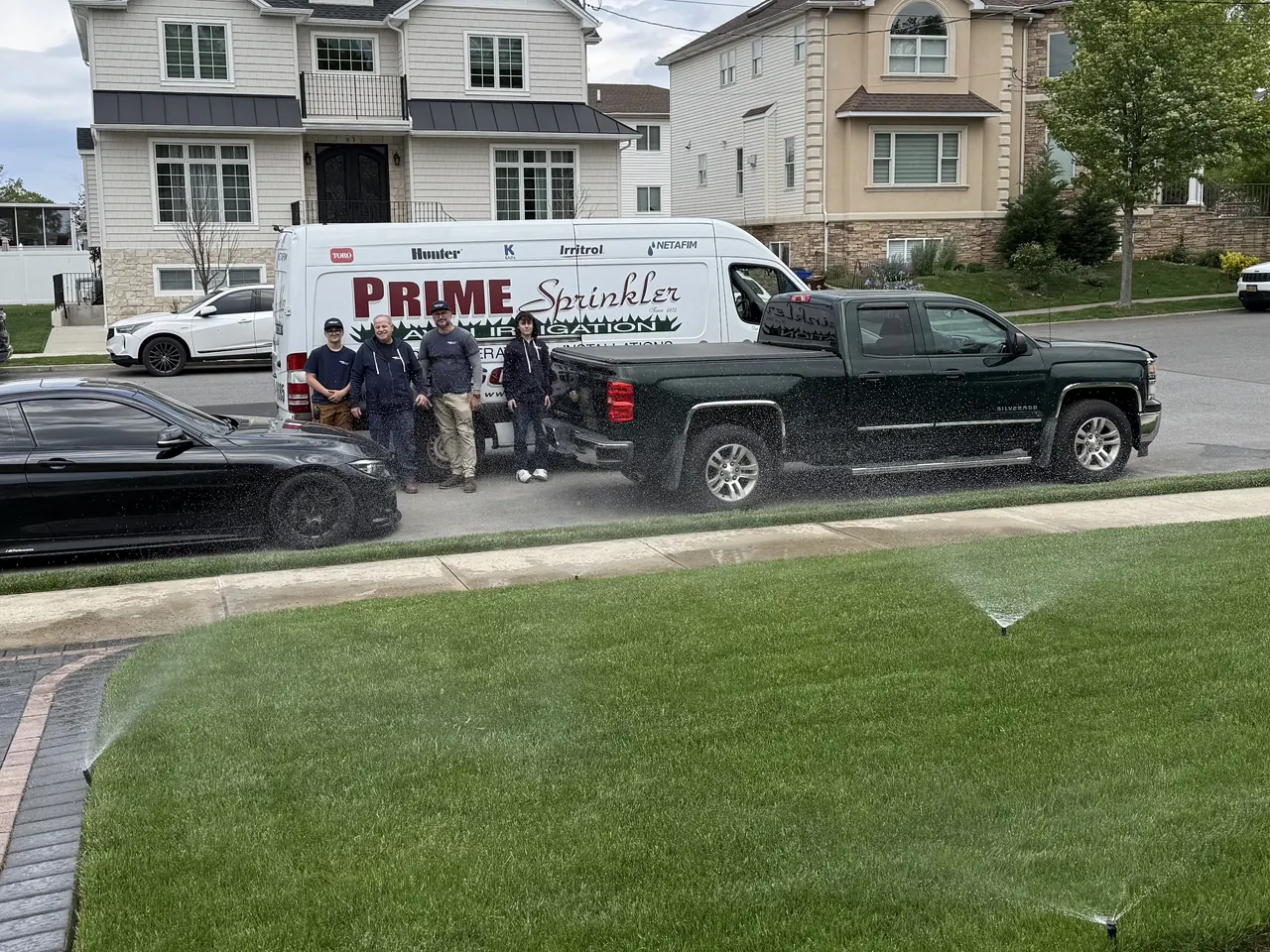 Prime Sprinkler crew standing beside the service truck in front of a finished lawn